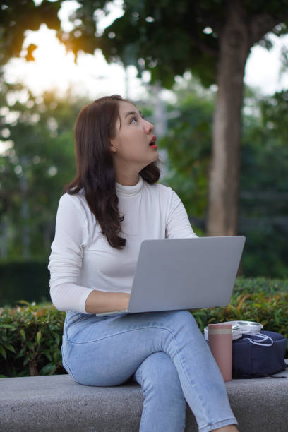 istock Cute young Asian female student working on a laptop computer outdoors, studying concepts, working in the public domain. 1388708842