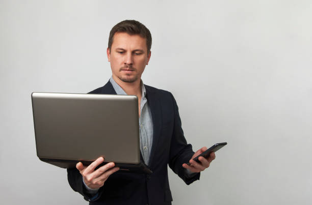 istock Young businessman using laptop and phone on white background 1388717139
