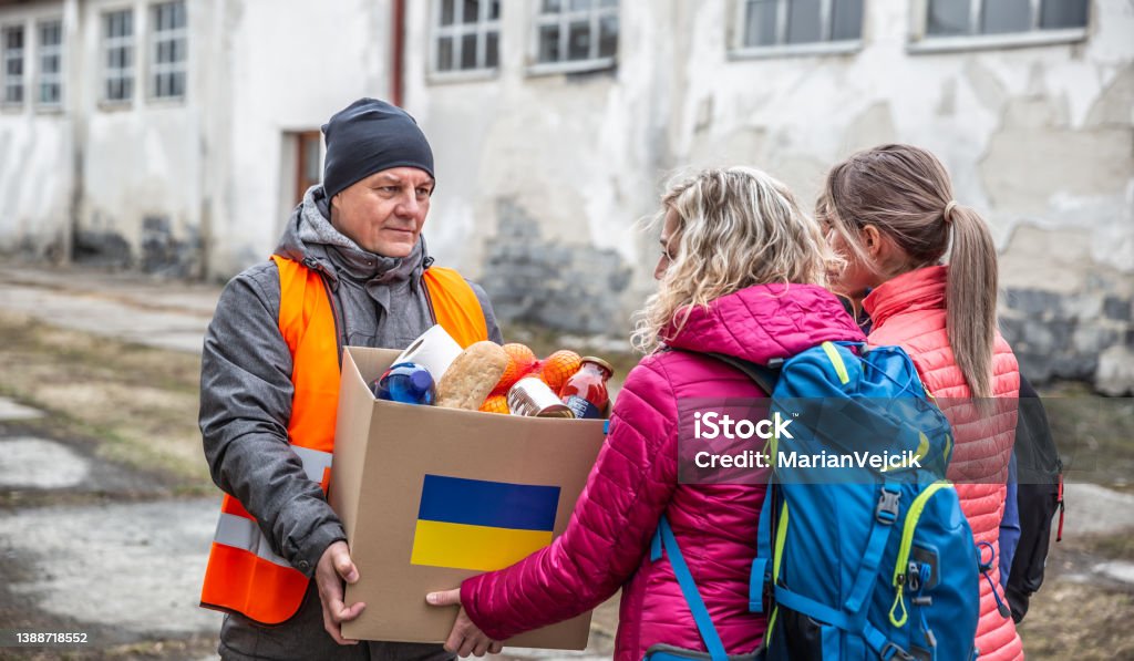 Volunteer in orange west gives a box of food donation to fleeing refugees from Ukraine. Ukraine Stock Photo