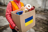 NGO volunteer carries a box with basic food and toilet papier with a Ukrianian flag sticker on the cardboard.