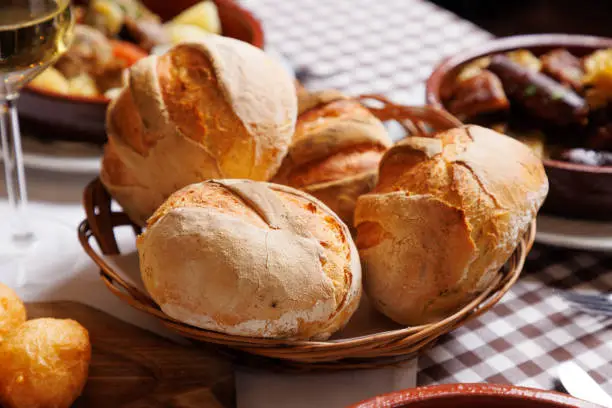 Crusty baked bread buns in wicker basket on ethnic restaurant table, traditional specialties buffet