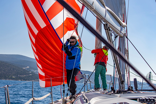 Sailing crew on sailboat during regatta. Men enjoying aquatic sport and togetherness. Skipper and sailors on sailboat at yacht race. Sports team navigating sail ship in motion. Nautical activity background with space for advert text, poster or banner.
