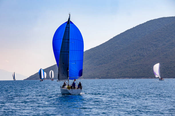 Sailboats sail in windy weather on blue waters of the Aegean Sea. Sailing crew racing at regatta. Yacht boat with mast. Water splashes, islands, sky and seascape background with copy space.