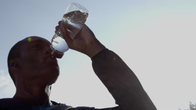 4k video footage of a young man taking a break fro jogging to drink water