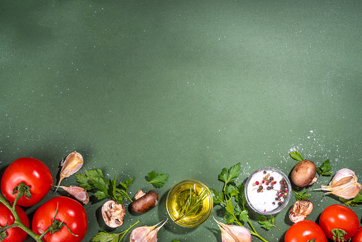 Food cooking preparation background. Kitchen table background with spices, herbs, vegetables. Parsley, onion, garlic, tomatoes, salt, olive oil on dark green  background top view flatlay copy space
