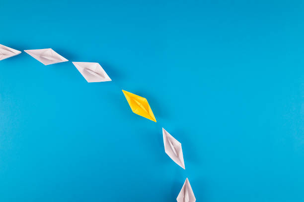 istock Group of White Paper Boats with One Yellow Boat Going Same Direction 1388725513
