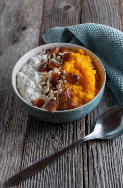 Fitness breakfast bowl with high protein cottage cheese, pumpkin puree, dates and nuts. Served with spoon isolated on wooden table with "copy space"