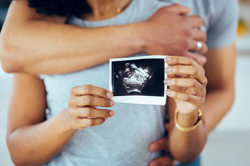 Pregnant couple feeling happy show ultrasound image at home, focus on ultrasound image