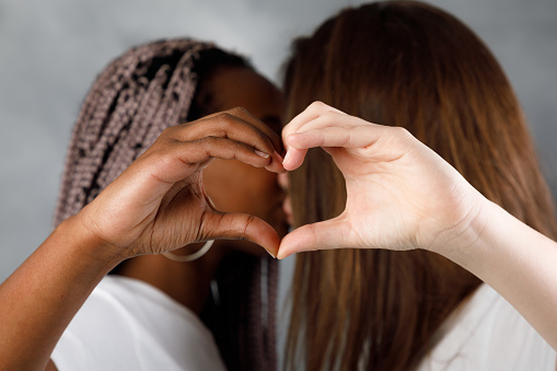 Two girls making a hand heart. Multiethnic lgbt couple.