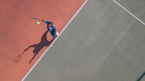 punto de vista del dron Jugador de tenis asiático sirviendo la pelota con sombra directamente encima photo