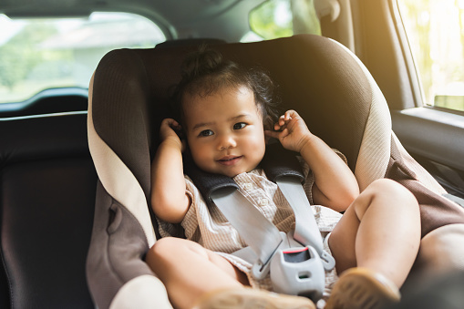 Baby Toddler girl sitting in car seat sit near window. Infant baby with safety belt in vehicle. Safety car. Family travel concept