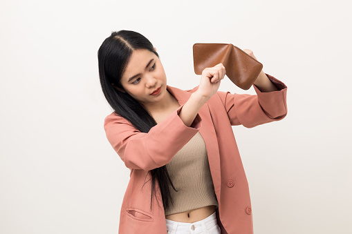 Asian business woman looking at empty wallet. Flip it over but don't have money inside wallet. Standing on isolated white background.