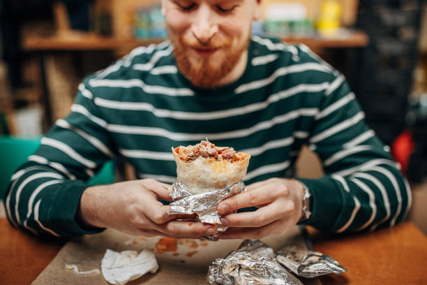 hombre comiendo burritos - burrito fotografías e imágenes de stock