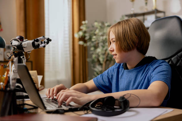 istock Smart smiling ambitious boy sits at desk in front of laptop looking at robot he is testing, teenager prepares for online robotics class, e-learning, extra lessons, developing passion hobby 1388731651