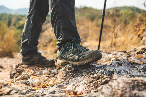 Close up mountaineering boots walking on rocky mountains at  outdoor. Tourist walks on adventure trip in natural at holidays. Travel lifestyle concept