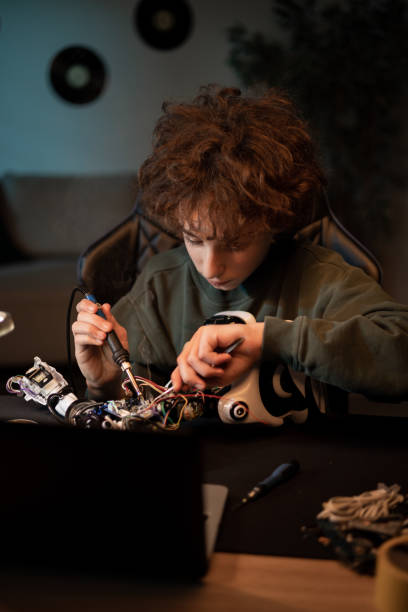istock The boy spends time at home at desk digging into the electronics that power the robot, pulls out wires with a tweezers and solders them tutorial instructions in laptop 1388731809