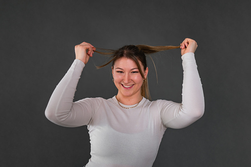 Portrait of a young cheerful woman in a studio, touching her hair.