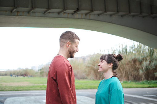 A young couple stands outdoors and looks at each other.