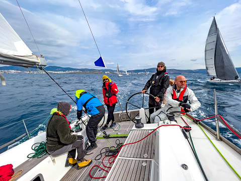 Sailing crew on sailboat during regatta. Men enjoying aquatic sport and togetherness. Skipper and sailors on sailboat at yacht race. Sports team navigating sail ship in motion. Nautical activity background with space for advert text, poster or banner.