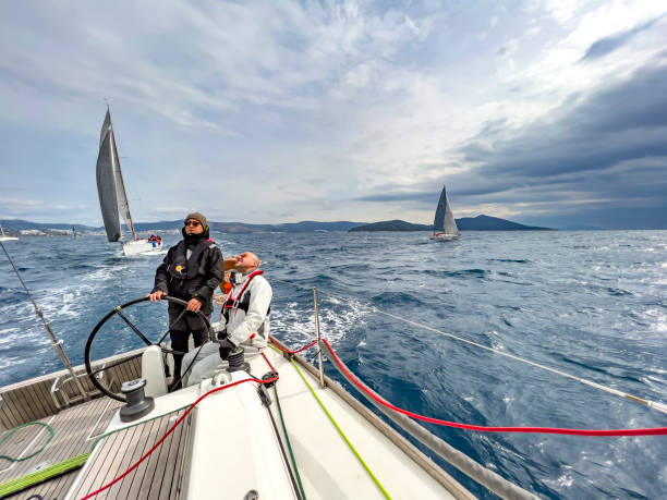 レガッタでレースするヨットのデッキ上の舵取り船長と男性船員、空は背景を見る - sailing ship sailing rudder sailboat ストックフォトと画像