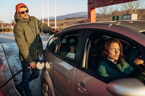 A millennial woman is waiting for her boyfriend in the car while he fills the tank of his car