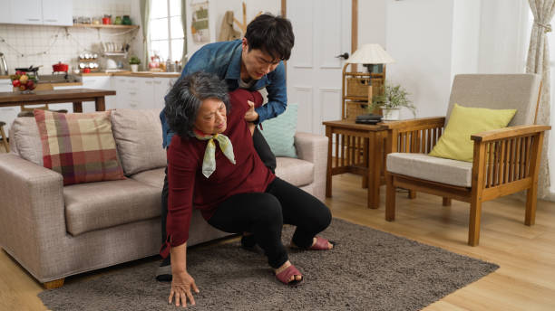 Asian adult son quickly come over to help his retired mother sit and rest on sofa after a fall on floor at home. He put cushion behind her back to make her feel better Asian adult son quickly come over to help his retired mother sit and rest on sofa after a fall on floor at home. He put cushion behind her back to make her feel better put down stock pictures, royalty-free photos & images