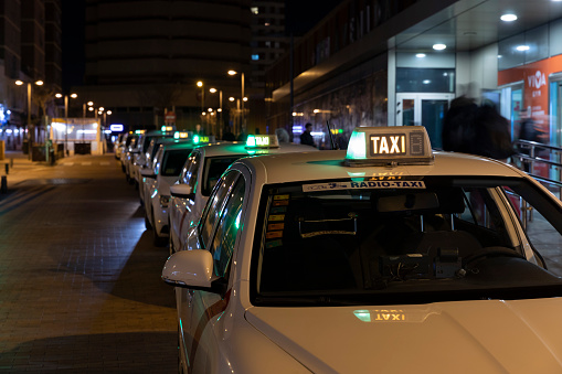 Row of Spanish cabs parked in the cab parking on avenida america in Madrid at night with green lights on.