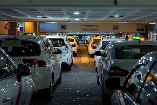 Row of Spanish cabs parked in the cab parking at Chamartin train station in Madrid at night with green lights on.