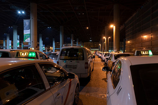 Row of Spanish cabs parked in the cab parking at Atocha train station in Madrid at night with green lights on.
