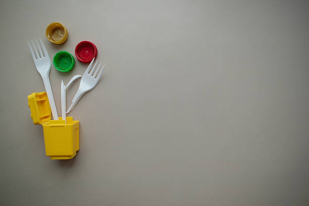 istock sticking out of a yellow garbage container: a broken plastic fork, multi-colored bottle caps, on a plain background, top view, free space 1388752392
