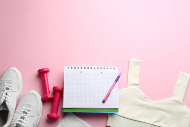istock Flat lay composition with sportswear, notebook and dumbbells on pink background, space for text. Gym workout plan 1388755336