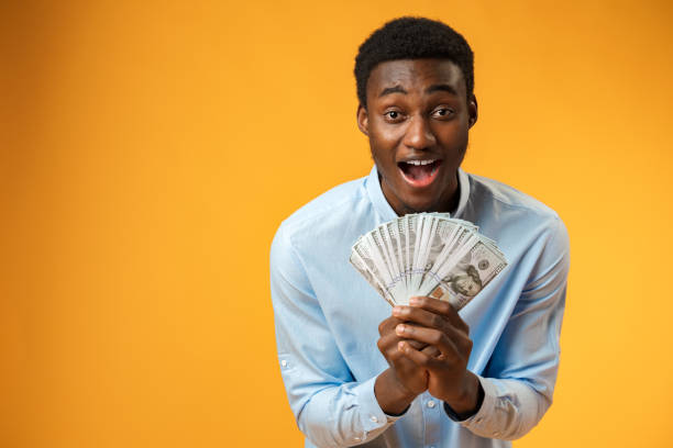 istock Excited black guy holding stack of Dollars in yellow studio 1388756417