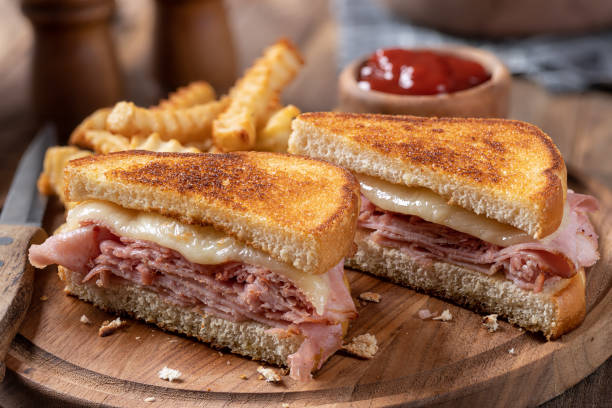 Grilled ham and cheese sandwich with french fries Grilled ham and cheese sandwich cut in half with french fries on a wooden cutting board toasted sandwich stock pictures, royalty-free photos & images