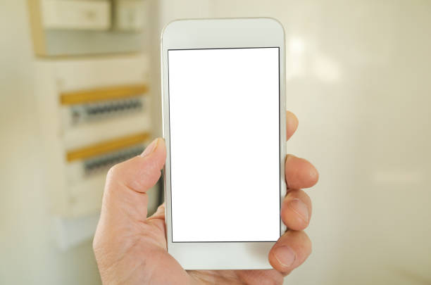 POV shot using a smart phone with blank screen next to electricity meter and fuse box - for e.g. smart home automation application, meter reading, controlling energy usage. White screen for insertion of graphic.