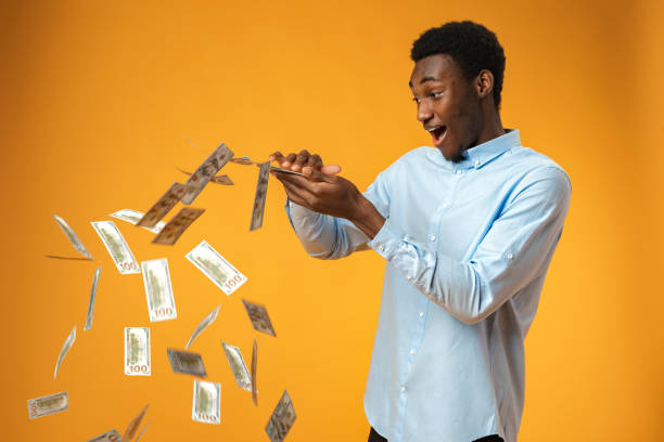istock Excited black guy holding stack of Dollars in yellow studio 1388760401