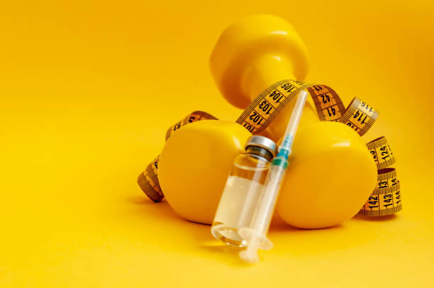 syringe and jar of liquid lie on dumbbells with a measuring tape on a yellow background, a horizontal picture. the concept of doping in sports, steroids, testosterone and other drugs for weight loss. syringe and jar of liquid lie on dumbbells with a measuring tape on a yellow background, a horizontal picture. the concept of doping in sports, steroids, testosterone and other drugs for weight loss. anti doping stock pictures, royalty-free photos & images