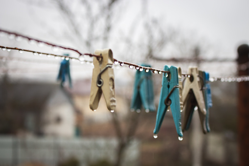 Clothes pins on wire. Rope with pins and raindrops. Laundry concept. Rainy day in village. Rural still life. Water drops and pins close up. Countryside landscape. Spring weather concept.