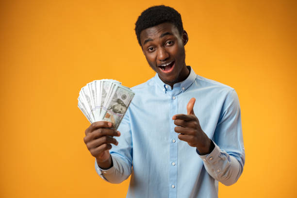 istock Excited black guy holding stack of Dollars in yellow studio 1388765796