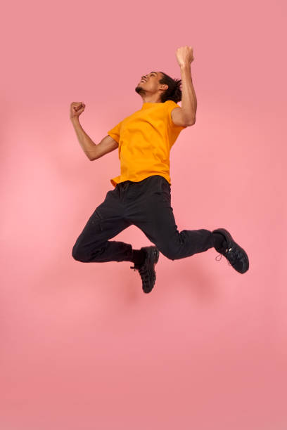 Full length shot of a cheerful funny black man in sneakers, crazy flying carefree jumping with raised arms, celebrating victory, having fun, rest, relax and leisure, isolated on pink background Full length shot of a cheerful funny black man in sneakers, crazy flying carefree jumping with raised arms, celebrating victory, having fun, rest, relax and leisure, isolated on pink background. air jump stock pictures, royalty-free photos & images