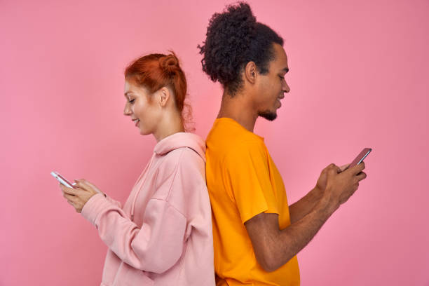 Red haired woman, handsome dark skinned man standing back to back writing messages through internet