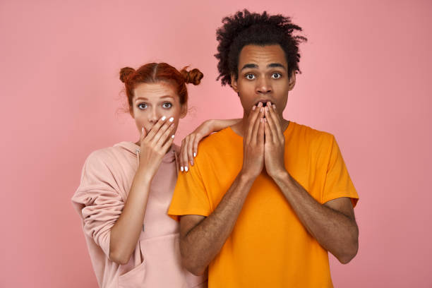 istock Frightened young couple cover mouths with hands, keep eyes popped out 1388767576