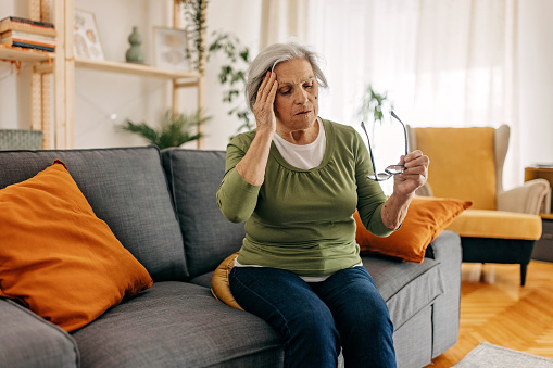 Older woman having headache, sitting at home and trying to relax