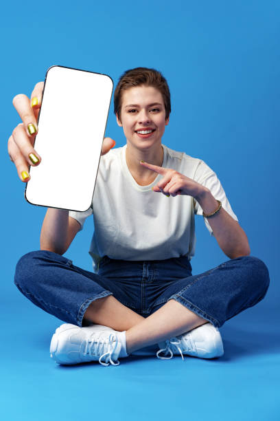 istock Happy woman shows blank smartphone screen against blue background 1388772671