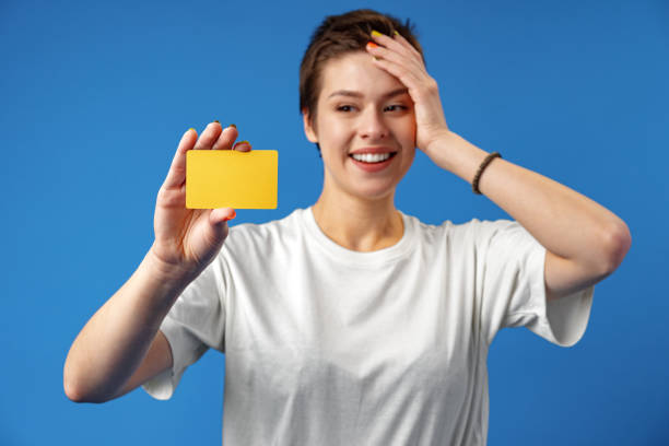imagen de una mujer joven sosteniendo una tarjeta de visita con espacio de copia sobre fondo azul - invitation blank smiling business card fotografías e imágenes de stock