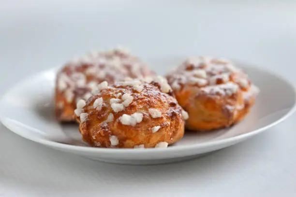 Small cream puffs on a white plate with pieces of sugar