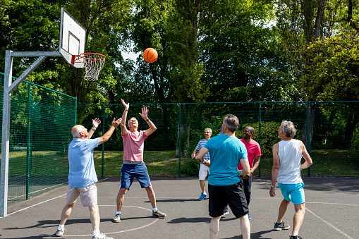A group of senior men enjoying a day out together and playing basketball at a basketball court in Newcastle-Upon-Tyne, England. They are all watching the basketball in the air after a man has thrown it.