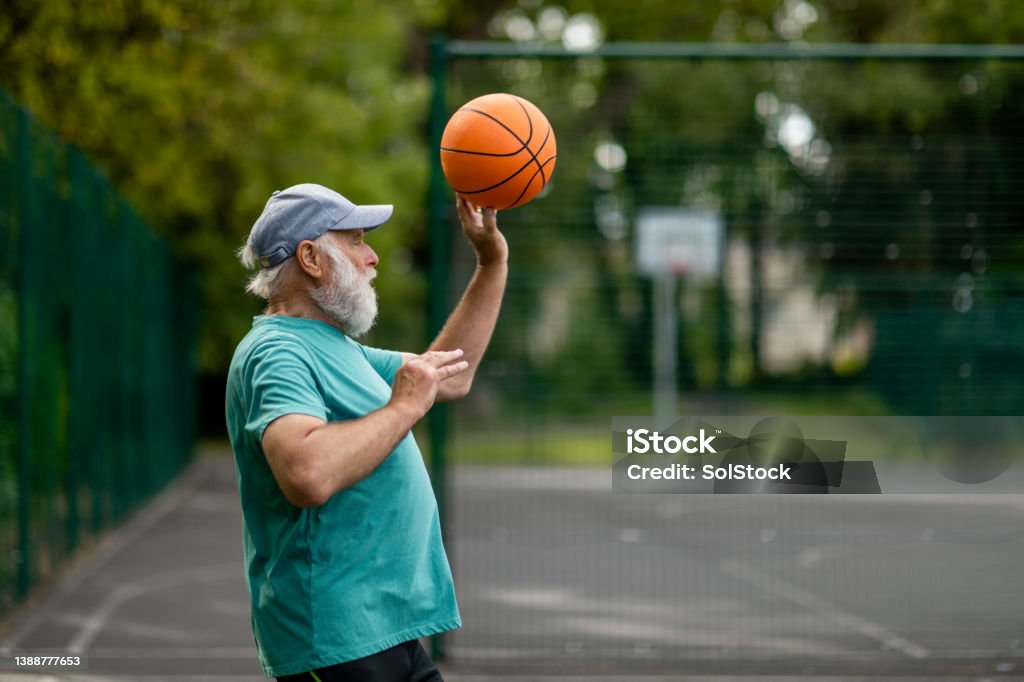 Passing to a Teammate A senior man throwing a basketball on a basketball court in Newcastle upon Tyne. He has his arms raised during mid throw. Basketball - Ball Stock Photo