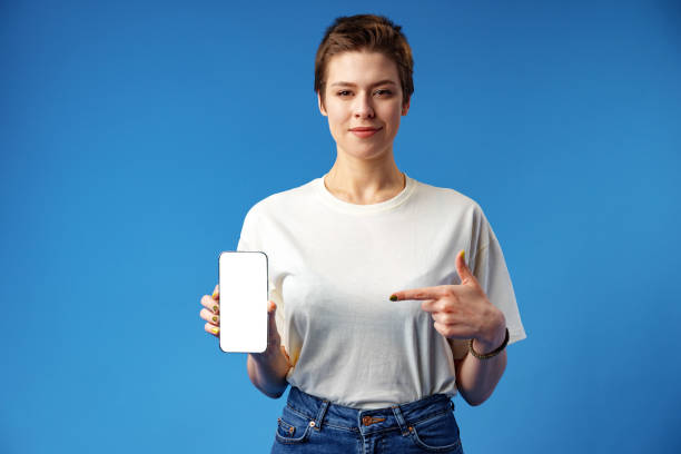 istock Happy woman shows blank smartphone screen against blue background 1388779128