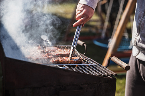 Man grilling meat on a barbecue party at his backyard