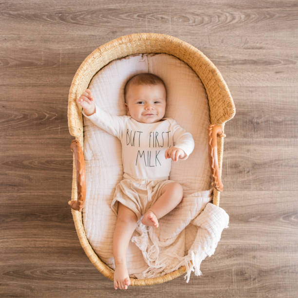 A Happy 14 Week Old Baby Boy Wearing a White Onesie With the Words 'But First Milk' Laying in a Cozy Cream Cotton Blanket in a Seagrass Moses Basket A 14 Week Old Baby Boy Wearing a White Onesie With the Words 'But First Milk' Laying in a Cozy Cream Cotton Blanket in a Seagrass Moses Basket moses basket stock pictures, royalty-free photos & images